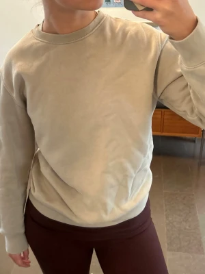 Beige sweatshirt utan huva - En enkel och stilren beige sweatshirt med rund halsringning och långa ärmar. Tröjan har en avslappnad passform och är tillverkad i mjukt material, perfekt för en chill och casual look. Inga synliga loggor eller tryck. Storleken är kids, 13-14 år (164 cm) men passar mig som är vuxen och 168 cm.
