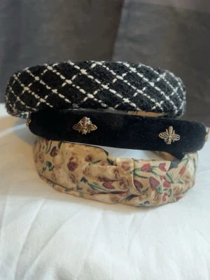 3-pack trendiga diadem i olika stilar - Säljer ett set med tre snygga diadem: ett svart och vitt rutigt i tweed, ett svart sammetsdiadem med guldfärgade biet-detaljer och ett beige diadem med blommigt mönster. Perfekta accessoarer för att lyfta din look och matcha olika outfits.