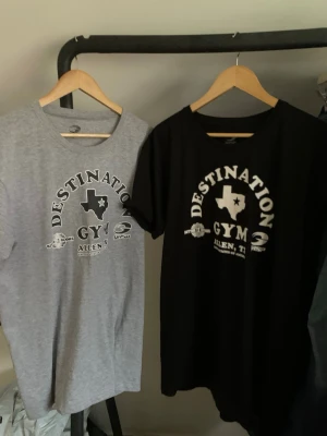 Destination Gym Texas t-shirts - Två t-shirts från Destination Gym med tryck av Texas och texten 'Destination Gym Allen, TX'. En är grå och en är svart, båda med rund hals och korta ärmar. Perfekta för gymmet eller chill dagar. Hör av dig vid minsta fundering och pris kan diskuteras! 🤩💯
