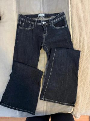 Mörkblå bootcut jeans från Jack & Jones - Säljer ett par mörkblå bootcut jeans från Jack & Jones med kontrastsömmar och klassisk femficksmodell. Jeansen har en låg midja och är tillverkade i kraftigt denimtyg. Perfekta för dig som gillar en avslappnad men ändå snygg stil.