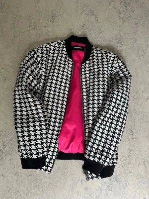 DSQUARED2 - Houndstooth mönster - svart vit rosa - Säljer en DSQUARED2 bomber jacka med hundtandsmönster. Jackan har svart ribbad mudd vid ärmslut, krage och nederkant samt en snygg rosa insida.