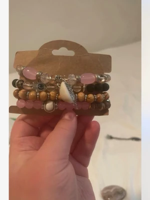 Set med pärlarmband i rosa och trä - Flera armband med pärlor i rosa rosenkvarts, träfärg och transparent. Några armband har silverfärgade detaljer och berlocker, inklusive snäckskal och öga. Perfekt för dig som gillar boho-stil och att mixa olika material och färger.