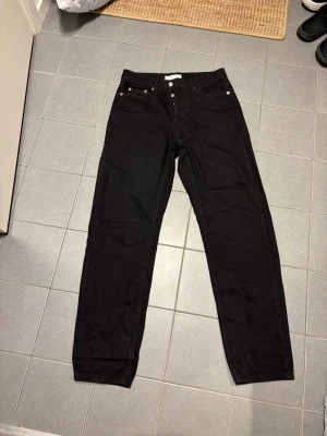 Svarta relaxed jeans från Topman - Säljer ett par svarta relaxed fit jeans från Topman. Klassisk femficksmodell med raka ben och knappgylf. Jeansen är tillverkade i ett slitstarkt denimtyg och har en stilren look som passar till det mesta.