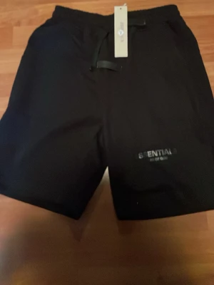 Svarta shorts från Essentials - Svarta shorts från Essentials Fear of God med diskret logga på vänster ben. Shortsen har elastisk midja med snörning och en avslappnad passform. Perfekta för en chill och stilren look. Står L men sitter som XS aldrig använda bara testat dem.
