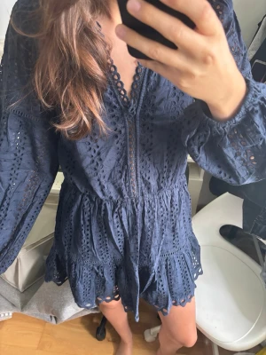 Mörkblå klänning  - Supersnygg mörkblå jumpsuit med långa ärmar och v-ringning. Tillverkad i ett luftigt spetsmaterial med broderade detaljer och vågig kant nertill. Aldirg använt 
