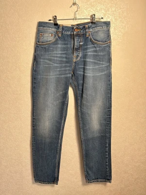 Nudie jeans Steady Eddie II - Snygga blå jeans från Nudie Jeans med klassisk femficksdesign och orangea sömmar. Jeansen har en rak passform och är tillverkade i denim med lätt slitning framtill och på bakfickorna. Perfekta för en avslappnad och trendig stil.🚨taggarna finns ej kvar🚨