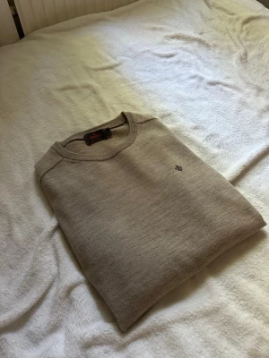 Beige Merino tröja från Morris - Snygg beige tröja från Morris med rund halsringning och diskret broderad logga på bröstet. Tröjan har en klassisk passform och är tillverkad i mjukt material som passar perfekt till lager på lager-stil.
