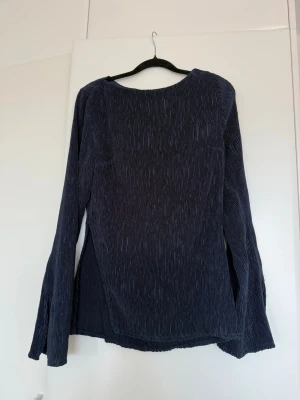 Mörkblått sett  i plisserat tyg - Säljer en mörkblå långärmad topp i plisserat tyg med rund halsringning. Tyget har en snygg struktur och toppen har en avslappnad passform. Perfekt att styla med matchande byxor eller jeans för en cool look.