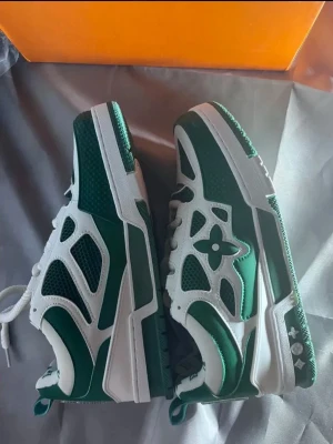 Gröna Louis Vuitton sneakers - Snygga gröna och vita sneakers från Louis Vuitton med ikoniska monogramdetaljer på insidan och LV-blomma på sidan. Skorna har en chunky sula, meshpaneler och vita skosnören. Perfekta för dig som vill sticka ut med exklusiv streetwear.