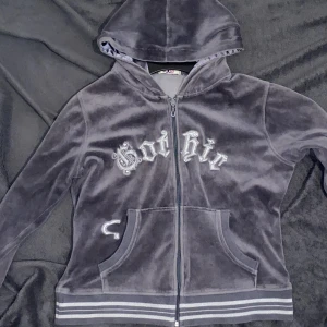 Grå velvet zip-up hoodie - En grå huvtröja i storlek dam L. Som referens är jag 165cm lång. Velvet material med glitter detaljer på texten och ränderna vid nedre delen av plagget.