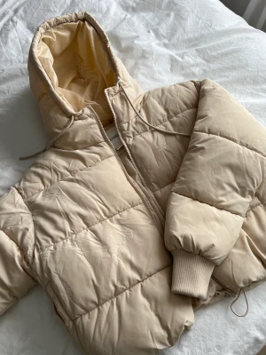 Cropped Puffer Beige - Använt totalt 3 ggr ute. Supermysig och varm puffer. Varmt innerfoder i fickorna och en dragsko  längs midjan av jackan.