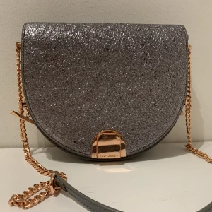 Ted Baker handväska  - Glittrig Ted Baker handväska köpt i London. Detaljer i rosa guld. Finns en skrapa på övre delen se bild 3 men det är inte något man lägger märke till 