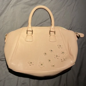 Ljusrosa handväska - Söt rosa/ beige handväska med detaljer. Den säljs då den inte matchar min stil men väskan är tålig och endast använd en gång. Bredden är 27 cm och höjden 23 cm  