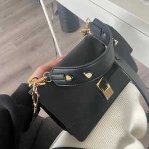 Svart väska - Säljer denna super snygga väskan då jag inte längre använder den. Den är i fint skick och väldigt rymlig. Enda defekten är dock är att ena ringen har lossnat som man ser på andra bilden till vänster men den funkar hur bra som helst utan den. 