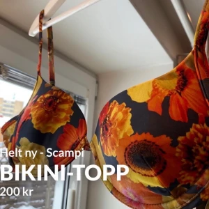 Scampi bikinitopp röd/orange blommor - Helt ny bikini topp från märket Scampi Deluxe. Storlek står M, men passar mer som S/M beroende på bröststorlek. Passar troligen A/B kupa bra. Är inte push-up modell och har bygel. Går att justera i både axelband och baktill. Nypris: 1000 kr