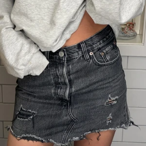 Jeanskjol  - Grå/svart jeanskjol med slitningar från Levis! Säljer då den inte kommer till användning, den är i storlek 24 men passar mig som har 34/36 annars. Köpte för 700 och säljer för 250🖤köparen står för frakten! 