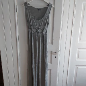 Grå långklänning från Urban Outfitters - Grå långklänning i jersey-material från Urban Outfitters med utstansade detaljer i midjan 