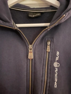Sailracing kofta - Jättefin, äkta sailracing ziphoodie i färgen marinblå. Aningen urtvättad.
