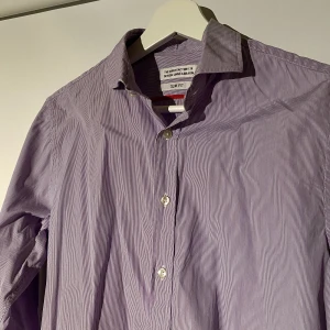 The Shirt Factory Skjorta  - Hej, säljer en lilavit randig skjorta från The Shirt Factory. Storlek 38 som motsvarar runt Small/Medium. Den är i utmärkt skick och perfekt nu inför studenttider. Nypris va 1199kr. Priset är inte hugget i sten. Hör av dig vid frågor.
