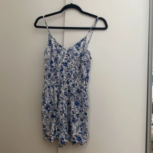 Blommig byxdress  - Jättesöt blåblommig byxdress med fickor. Skönt somrigt material. Söm i midjan som är stretch. Går att justera axelbanden. Shortsen blir mer som en kjol skulle jag påstå. Använd 1-2ggr.