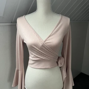 Top med V-skurning - En rosa top med v-skurning och knyte vid sidan och vida ärmar nertill. Storlek EU 38 och köpt på New Look i London.