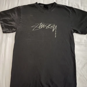 Stüssy T-shirt - Loose fit T-shirt från Stüssy i en washed out grå/svart färg med vit distorted logo. Sparsamt använd. 