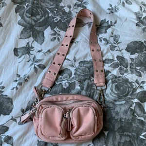 Rosa axelväska  - Riktigt fin axelväska, oanvänd. Köpte väskan för ett tag sen men den har bara legat bland de andra väskorna. Bra skick. Dragkedjorna på väskan funkar som de ska. Väskan är liten. 