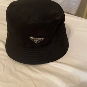 Prada Bucket Hat, Svart  - Ny skick, ej använd, nypris: 5300kr i affär där den var köpt  Jag säljer min Prada hat eftersom jag tyckte det var väldigt onödigt köp och har aldrig använt den, så vill bara få den såld. Priset jag säljer den för är 2500kr eller för någon skaplig trade  