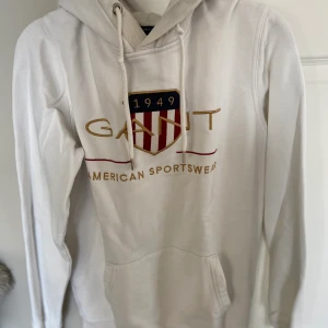 Vit Gant hoodie - Vit Gant hoodie  Storlek: small Hoodien är vit med tryck och fickor fram. Lågt pris pga en liten gul fläck på magen
