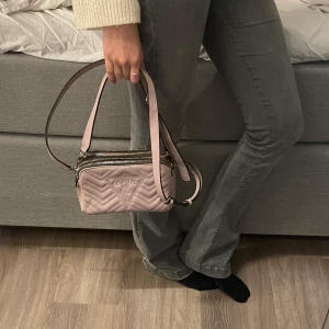 GUESS Väska - GUESS väska i jättefint skick👛. ÄKTA. Den är ljusrosa och har inga skador. Medföljer långt och kort justerbart band samt dustbag. Säljer för 280kr, pris går att diskuteras!💕. Hör av er vid frågor/fler bilder. Köparen står för frakten!! 