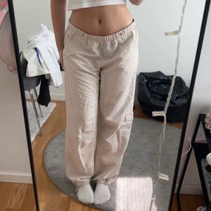 Byxor - Säljer dessa parachute/cargo byxor i beige. Storlek M men det går att justera midjan så passar även S. Även justerbara längst ner på benen. Sitter supersnyggt lågmidjat!!!! Frakt tillkommer på 51 kr spårbart! 