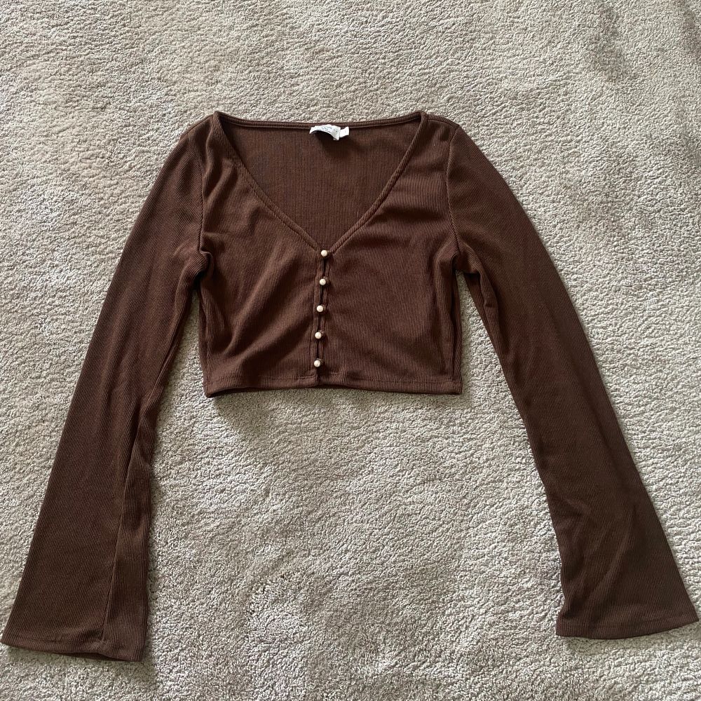 Brun topp från NA-KD, Hanna Schönbergs kollektion. Vida armar och kortare i midjan. Aldrig använd. Vita små knappar/pälor som man kan öppna och stänga. Storlek S.. Toppar.