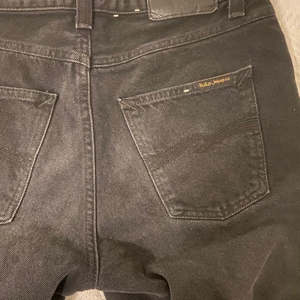 Svarta Nudie Jeans - Helt nya Nudie Jeans, använt en gång. Passformen är straight/regular fit.  Färgen är typ mörkgrå, de ser lite extra mörka ut på andra bilden.