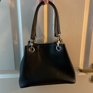 Svart handväska  - Svart handväska i vad jag skulle gissa är fake läder. Den är ca 16 cm hög.  Är köpt på humana. 