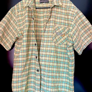 Oversize skjorta - En oversized skjorta från Rip Curl Surfwear med rutigt mönster. Ärmarna är kortärmade, men slutar vid armbågen på mig (163 cm lång och strl M). Extraknapp tillkommer. På vänstra bröstet finns en bröstficka med Rip Curls logga. Lite tjockare material än vad man förväntar sig av en skjorta, känns mer som bomull än polyestertyg. Köptes på en vintagebutik i Berlin och säljs pga flytt och därmed resning av garderob. Vintageplagg. 