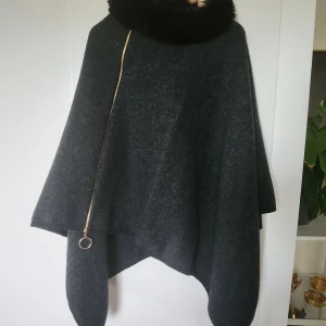 Ullponcho med pälskrage - Nyskick - Endast använd 1 gång. Är i nyskick. Jag är stl 34, men den skulle passa en 36a också. Den är i ull och äkta päls runt kragen (kanin). Nypris 2000 kr