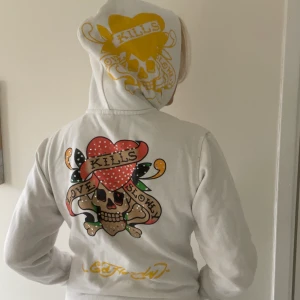 Ed Hardy vit zippup hoodie - Autentisk ed Hardy hoodie, köpt på plick. Detaljer av print och stenar. Mycket bra skick. Köpt för 500kr. Jag har normalt strl M och den passar mig bra. 