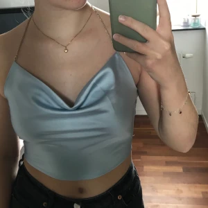 Tröja/linne - Ljusblå croppad tröja med avtagbar silverkedja i storlek S. Svårt att säga vilken bild som är mest rättvis mot färgen, typ en blandning av båda. Aldrig använd då jag inte hittat ett tillfälle att använda den. Har inte kvar prislappen men är helt oanvänd.