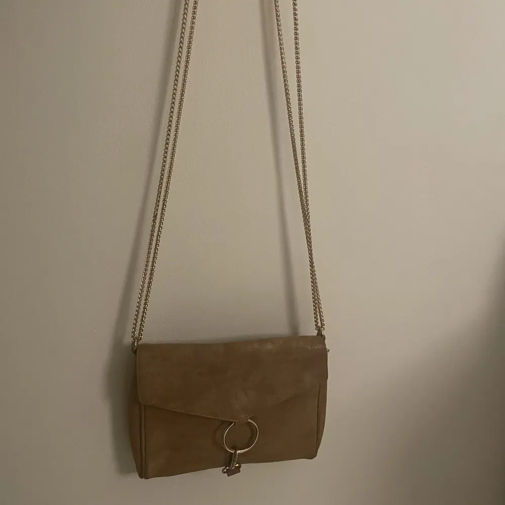 En handväska från gina tricot. Den är i färgen brun/guldinslag som syns bättre på andra bilden som är tagen med blixt. . Väskor.