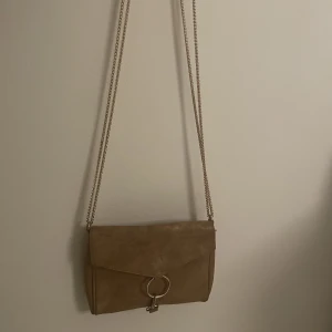Väska - En handväska från gina tricot. Den är i färgen brun/guldinslag som syns bättre på andra bilden som är tagen med blixt. 