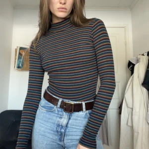 Randig turtleneck - En väldigt fin randig turtleneck i höstfärger som inte längre kommer till användning. Tight men stretchigt material! Den är i mycket bra skick, ser helt ny ut! Den slutar ungefär vid naveln. 70/80talet, hade lätt smält in i stranger things!