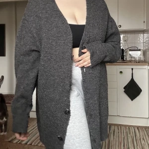 Grå kofta med knappar  - Grå kofta med knappar i storlek S från Bikbok.   Relativt nopprig i materialet men inget övrigt slitage på plagget. 62% akryl och 37% polyester samt 1% elastane  Slutar mitten på låret på mig som är 168cm. 