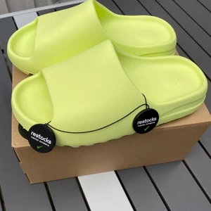 Yeezy slides Glow Green 2022 - Hej! Säljer mina slides på grund av att jag köpte fel storlek. Skorna är köpta på Restocks och de är helt oanvända. Tagen (brickorna) är kvar! Det visar att de är äkta. Skorna är lite små i storleken så den passsar 43-43,5. 