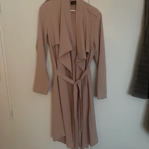 Rosa Kappa - Rosa kappa med snöre. Fickor, detaljer & jättefin!  Storlek XL, passar L/XL. Sista bilden ser man färgen bäst!