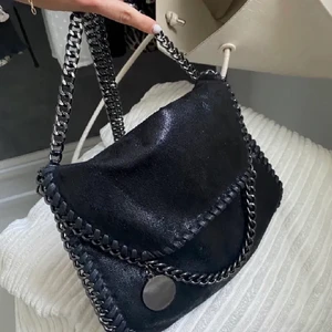 Väska - En svart skimrande Stella McCartney liknande väska. Den har två små fack i sidan och ett stor fack på andra sidan med dragkedja. Den är rymlig och skitsnygg. Har fått den och vet därmed inte vart den är från men det finns en liknande på Amazon för 500kr.