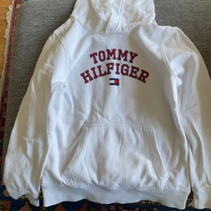 Tommy Hillfiget - Vit hoddy med huva och Tommy Hillfiger och tryck fram. Genomgående ficka på magen,
