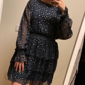 Festklänning med guldiga stjärnor  - Mörkblå volangklänning med guldiga stjärnor. Använd 1 gång och i nyskick