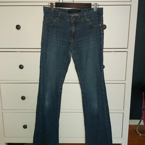 Calvin Klein Jeans - ett par lågmidjade "flare" jeans med strass på bakfickorna. en lagad sömn på baksidan, men som knappt syns. 80 cm från skrev -> ankel, ca 80 cm midja som vilar på höfterna. Köptes secondhand, men är knapp använda. Passar bäst för dig som har stl. 32/28 i byxor/jeans