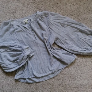 Cotton blouse with puffy sleeves - Cotton blouse with puffy sleeves, button closing and blue-grey stripes. Can be worn by someone who is between size S and XL. 