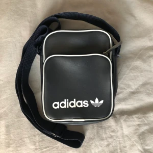 Adidas väska - liten mörkblå/grå (nästan svart) väska från Adidas. köpt 2017 för ca 300 kr. sparsamt använd & i bra skick! justerbara band.